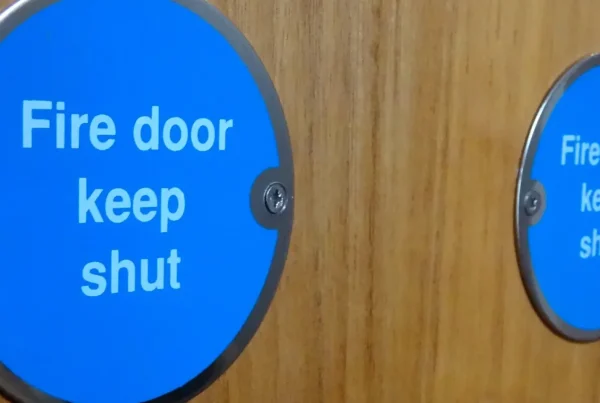 Close up of two blue circular metal plaques on two wooden doors saying "Fire door keep shut".