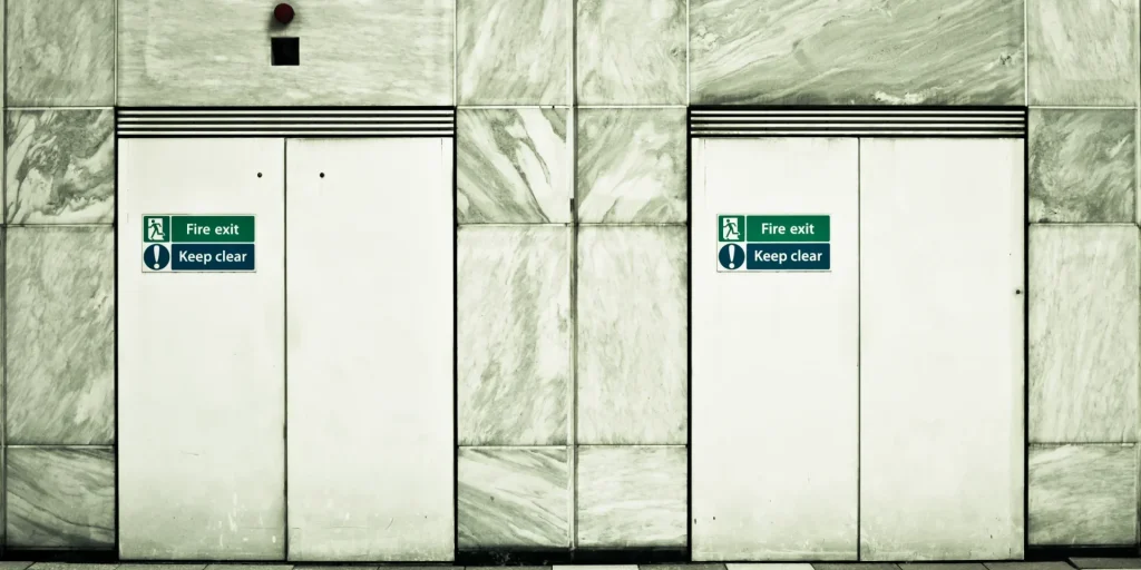 Two white double fire doors side by side, with alarbe marble-effct blocks surrounding them.