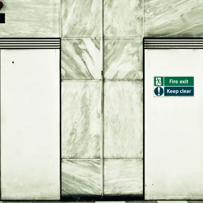 Two white double fire doors side by side, with alarbe marble-effct blocks surrounding them.