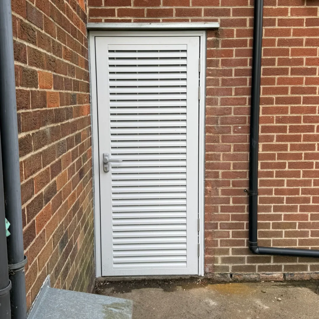 A white, slatted exterior door set in a red brick building