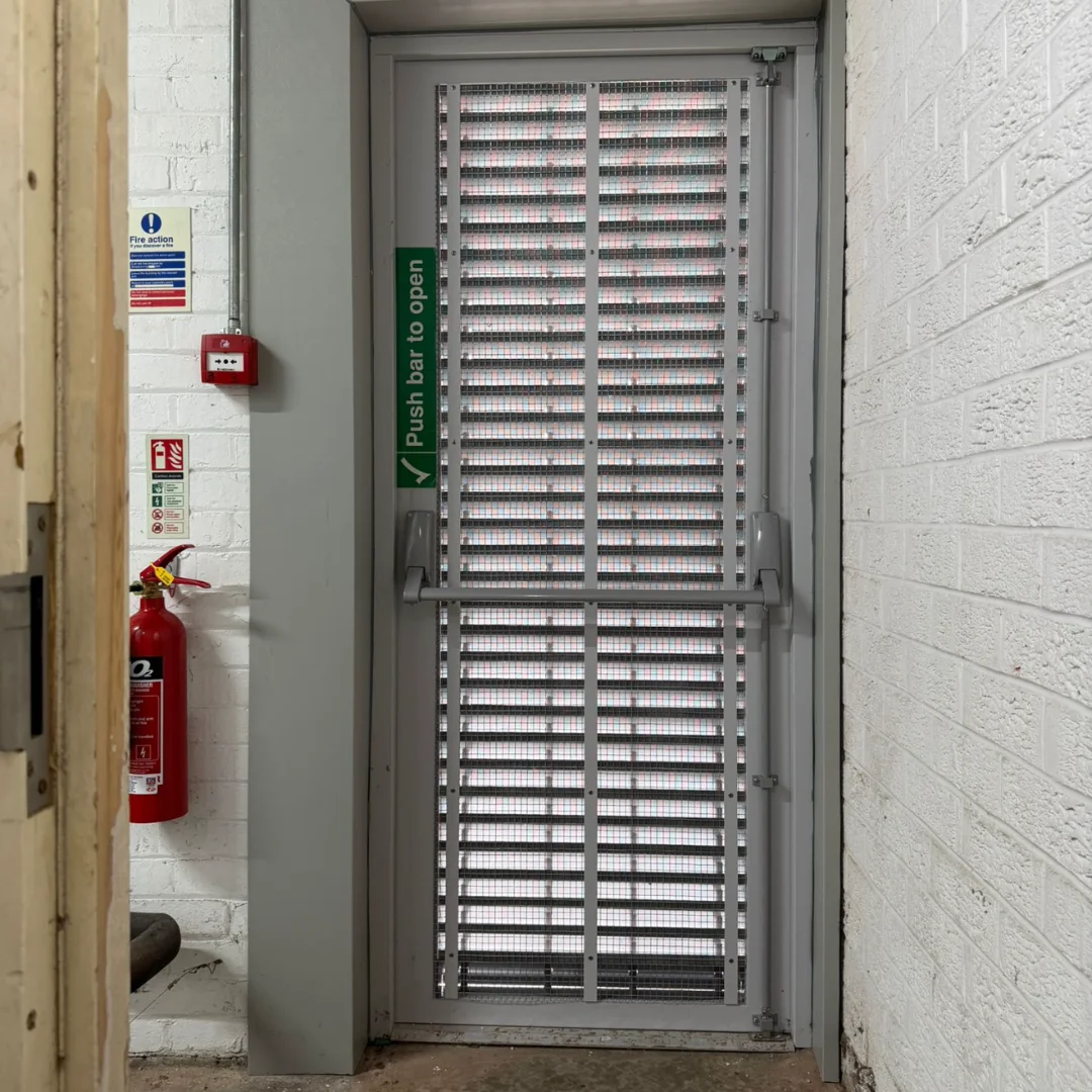 The interior of a slatted, ventialted fire door in a commercial premises with white walls