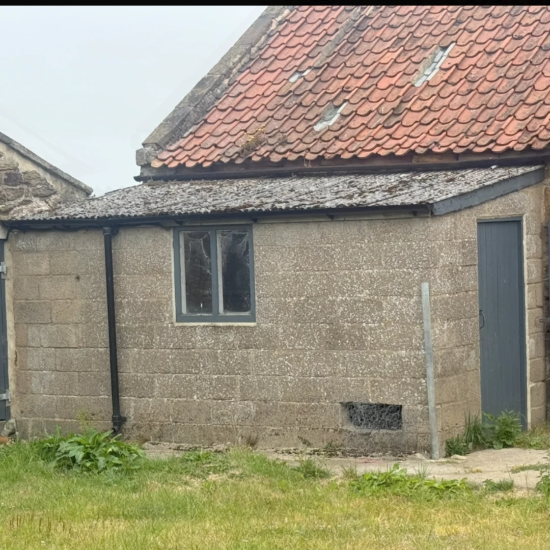 A breeze block-built outbuilding with an old asbestos roof.