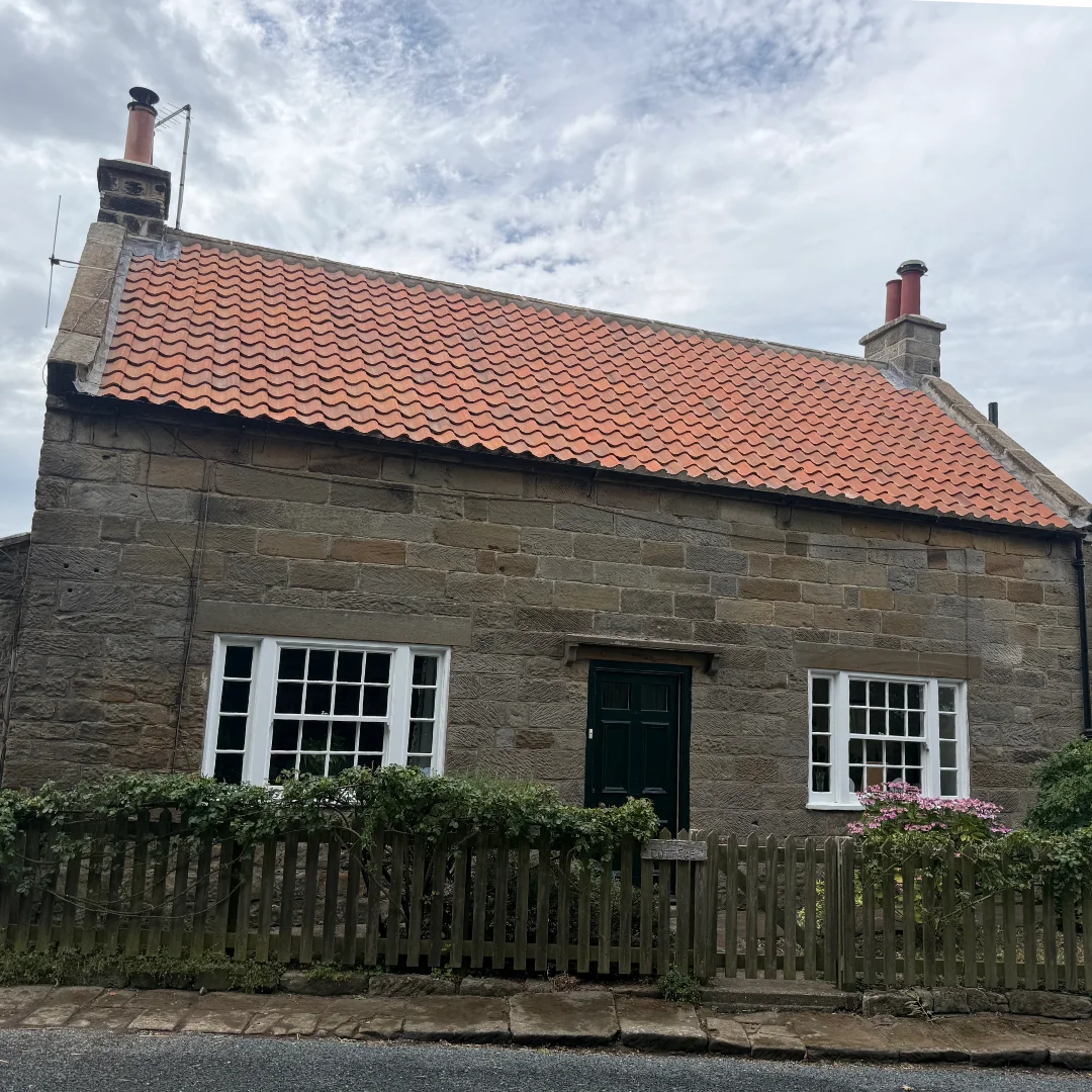 A traditional stone-built cottage with a red tiled roof, with the tiles looking refreshed after replacement.