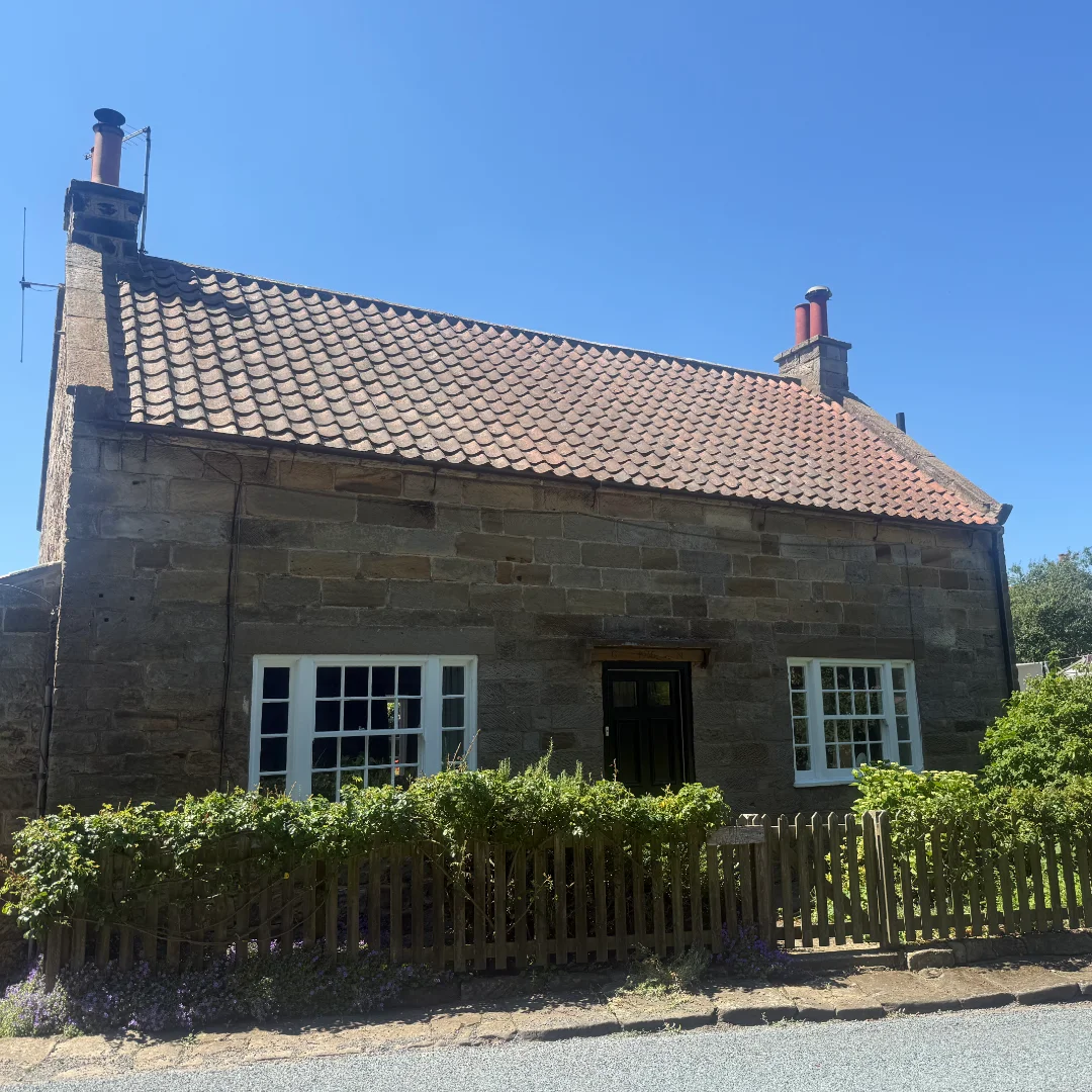 A traditional stone-built cottage with a red tiled roof, with the tiles looking tired and discoloured.