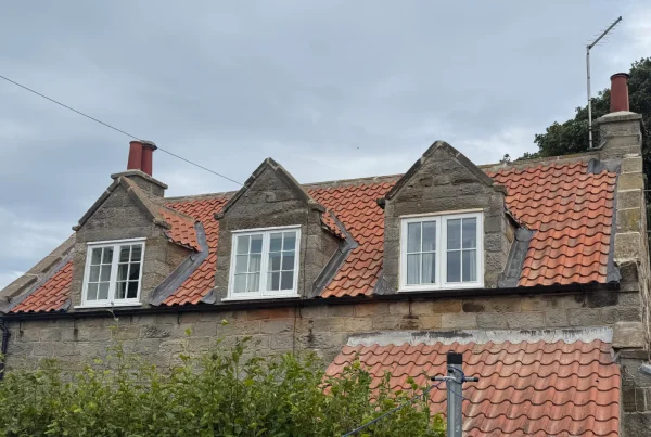 A photo of the rear of a traditional stone cottage, showing three dormer windows within the roof. The traditional red tiled roof has just been replaced.