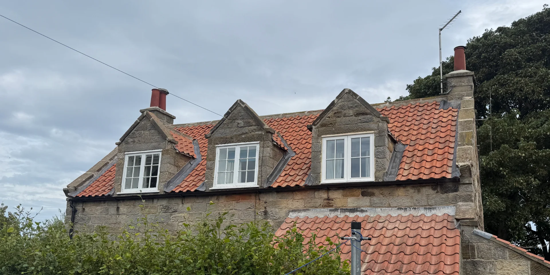 A photo of the rear of a traditional stone cottage, showing three dormer windows within the roof. The traditional red tiled roof has just been replaced.