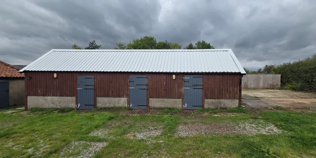 A brown wooden stable with three doors and a new, corrugated metal roof in a slivery-grey colour