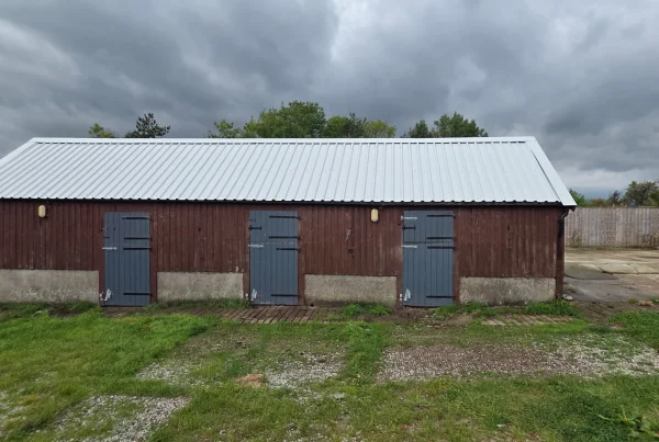 A brown wooden stable with three doors and a new, corrugated metal roof in a slivery-grey colour